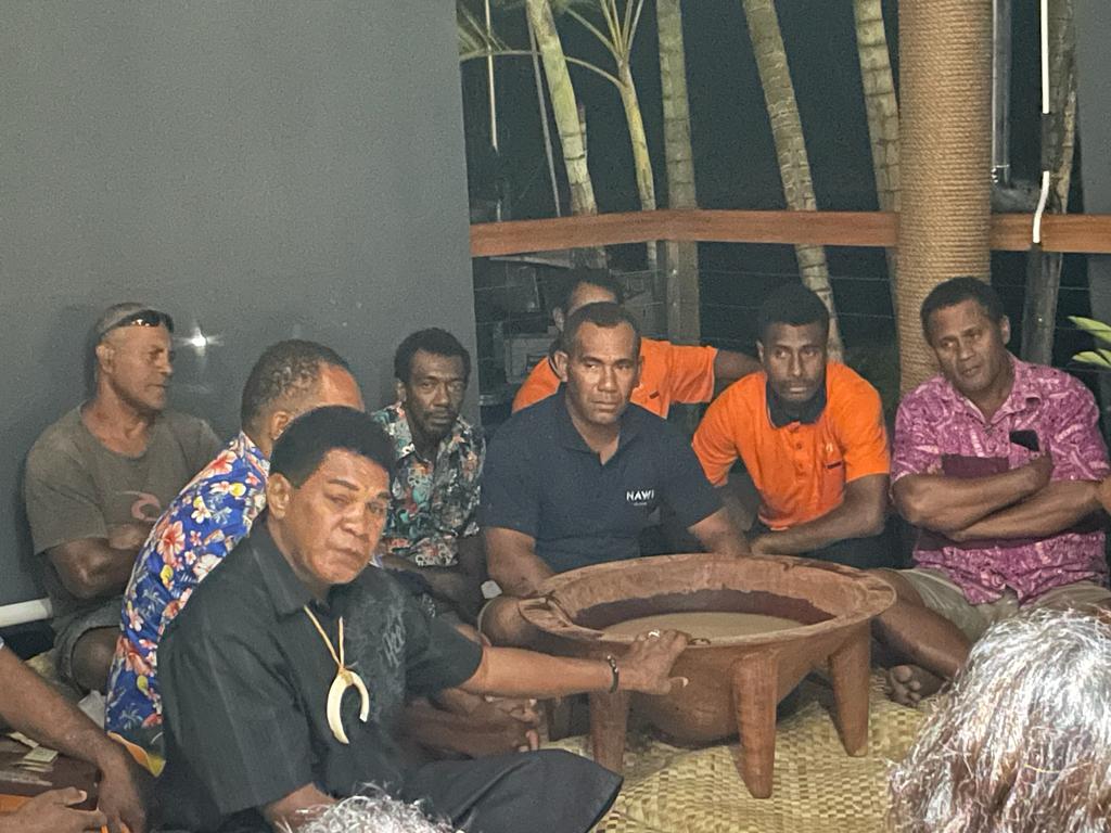Traditional sevusevu welcoming ceremony. A group of men with behind the chief who is wearing a boar tusk to indicate his status and lineage. A large bowl contains the kava drink.