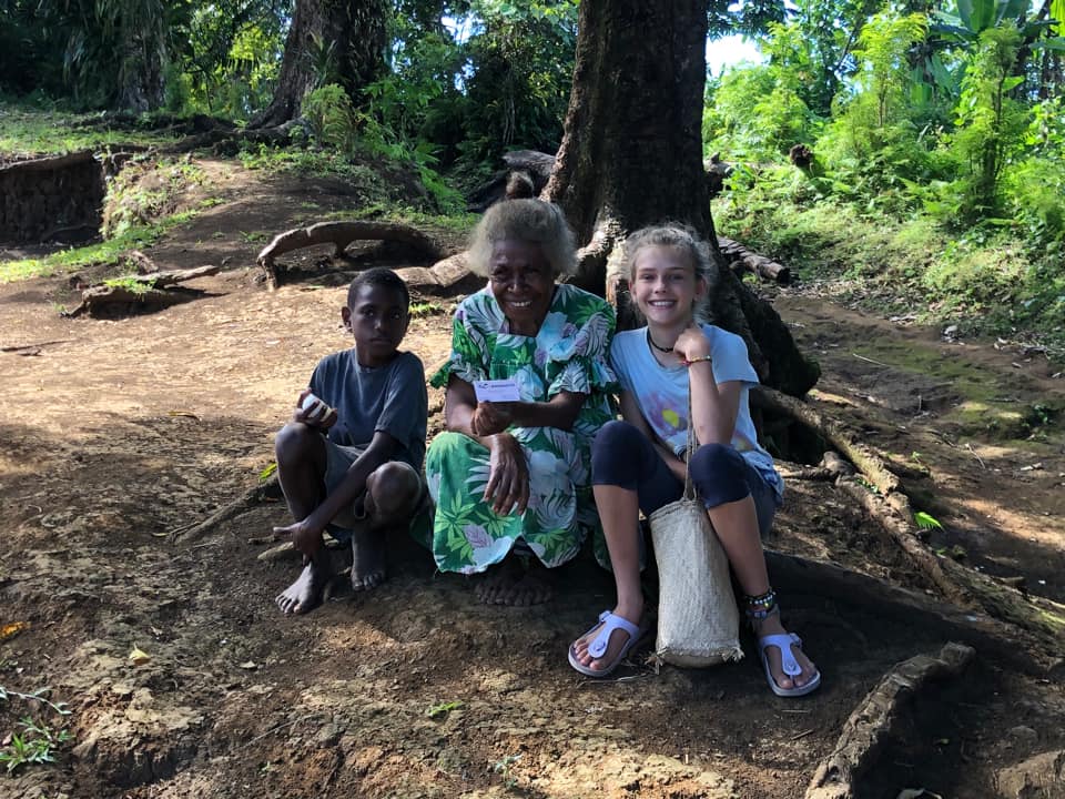 Margaret from Pentecost Island, Vanuatu, sitting outdoors with Karen and a local village boy under a large tree