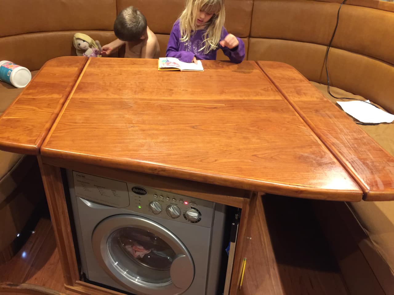 Henry and Karen with the Splendide washer/dryer on SV Aphrodite with the machine in its custom hutch under the saloon table